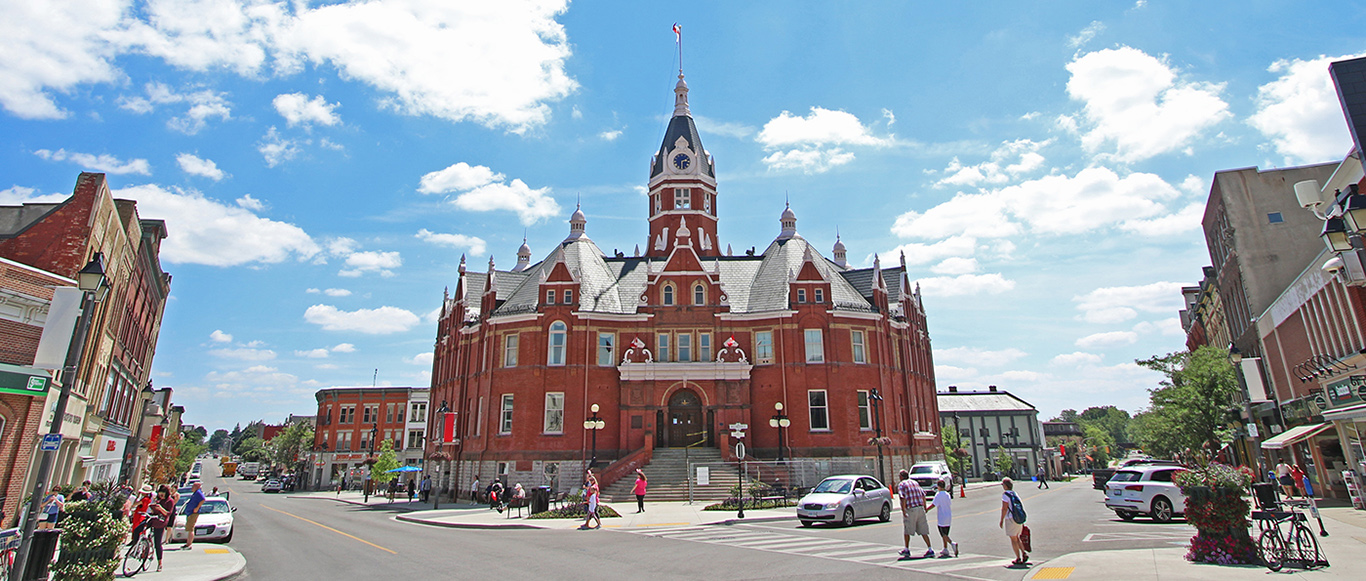 Image of downtown Stratford with City Hall at centre, with people crossing at an intersection