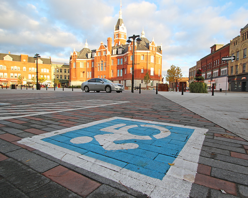 A dynamic accessibility parking sign with a silver car parked in front of Stratford City Hall