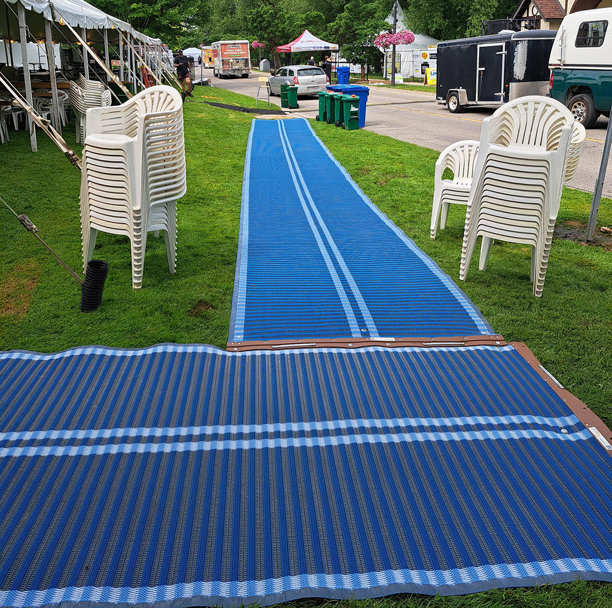 Blue mats laid on the grass, with tents and stacked white chairs.