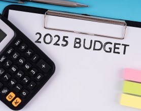 A calculator, coloured sticky notes and a clipboard with the words "2025 BUDGET" at the top.