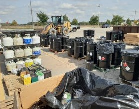 A parking lot with drums and containers of household hazardous waste